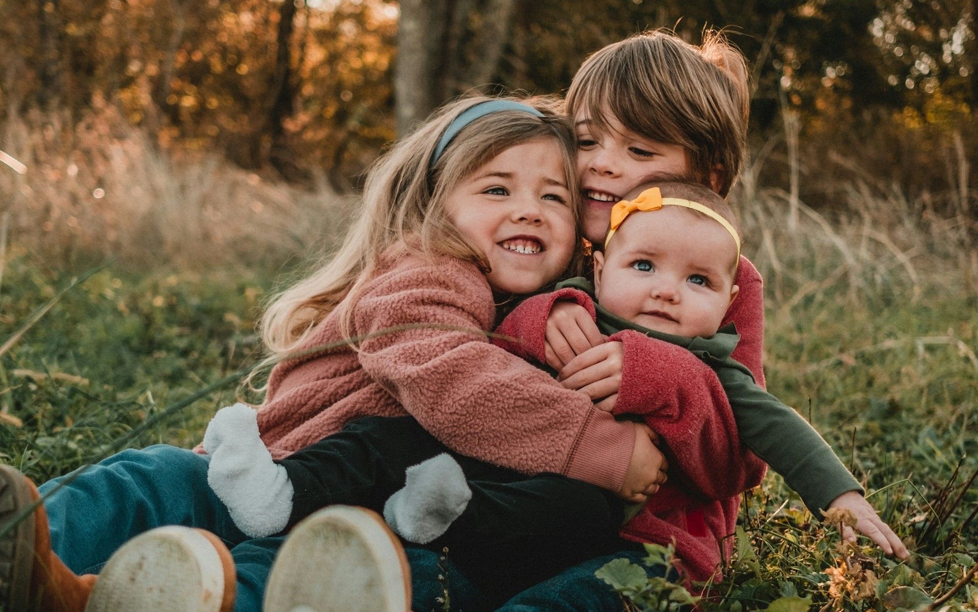 Three young children hug on a field.