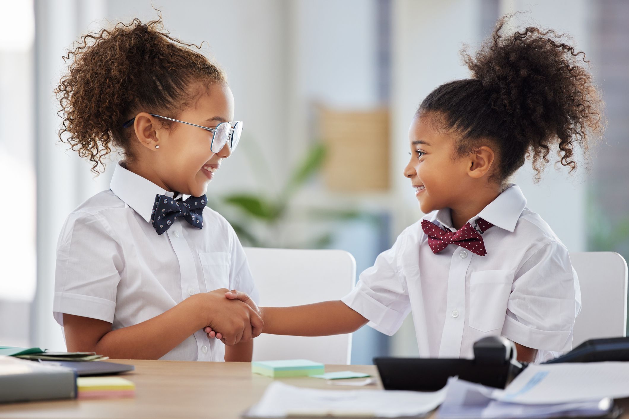 Two girls at primary school shake hands as if introducing themselves for the first time.