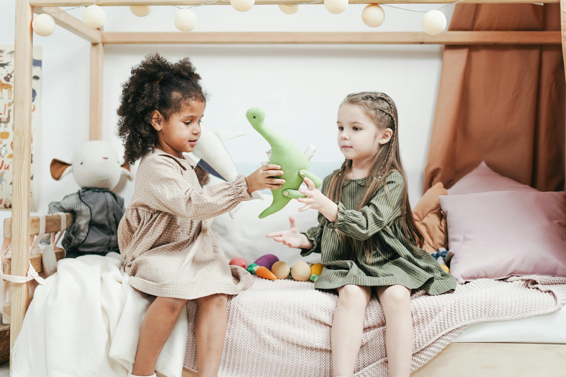 two kids sit on the side of the bed and share their dinosaur toy together.