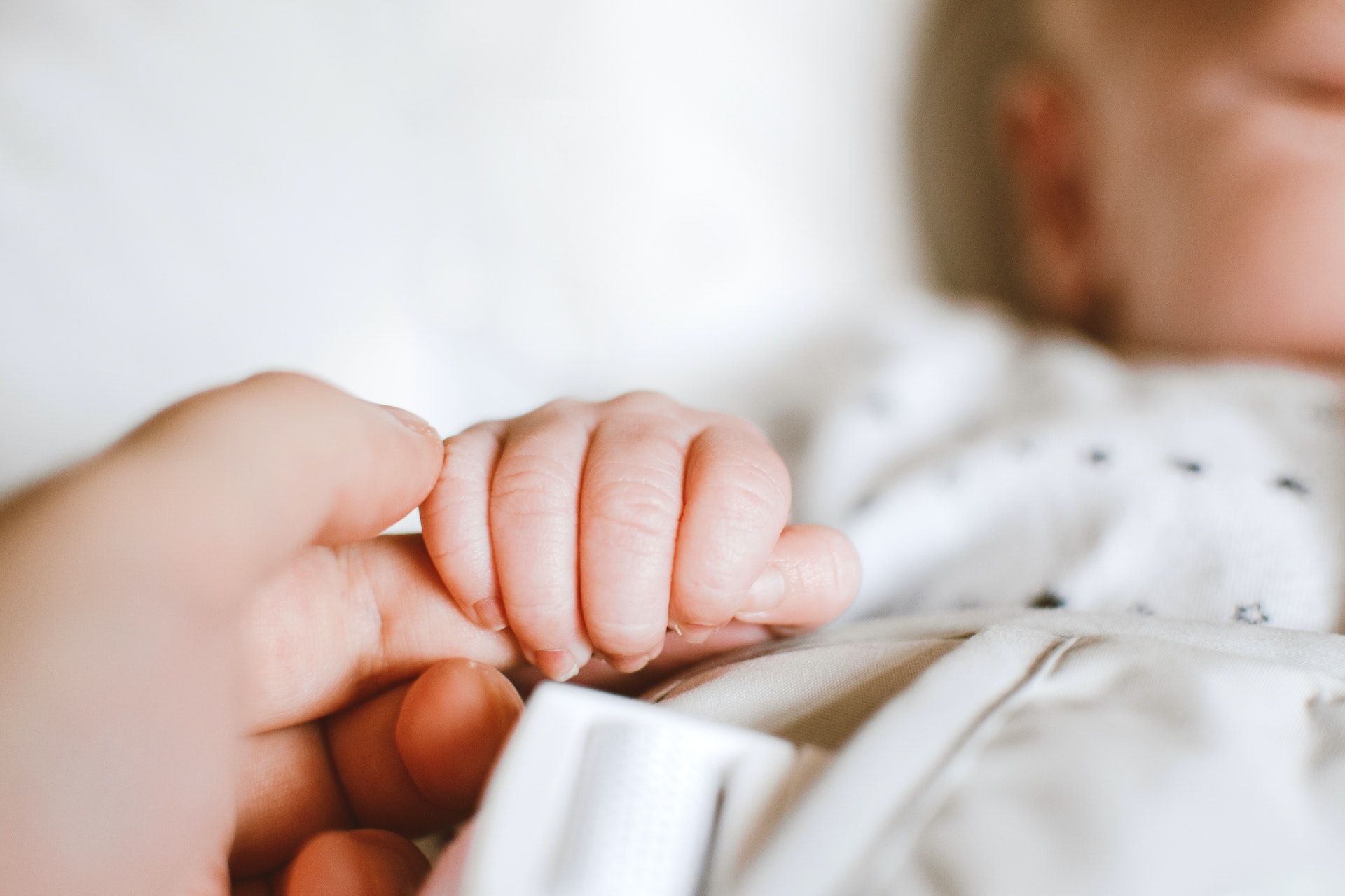 A baby squeezes their parents finger.