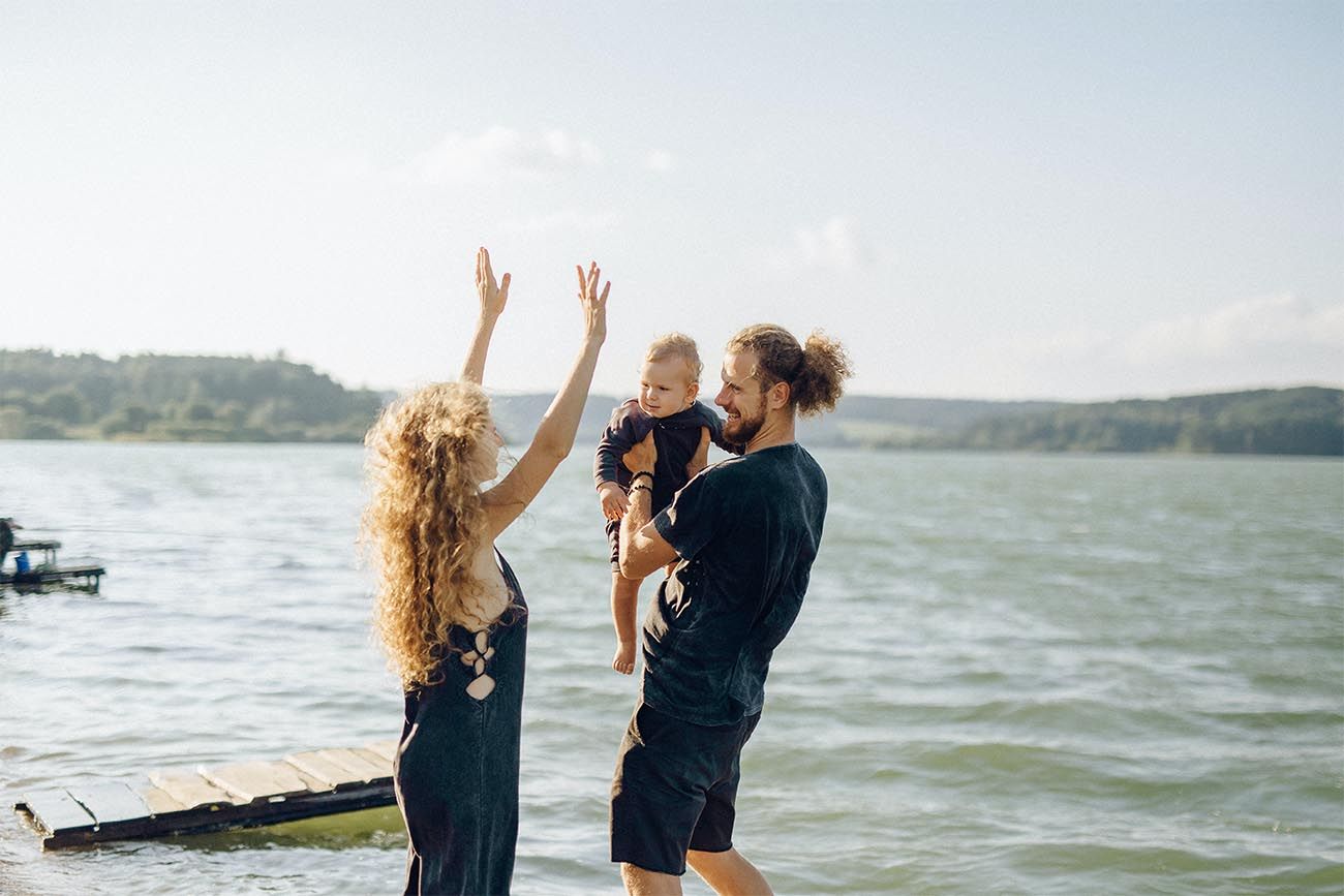 parents holding baby on the beach, with their arms in the air