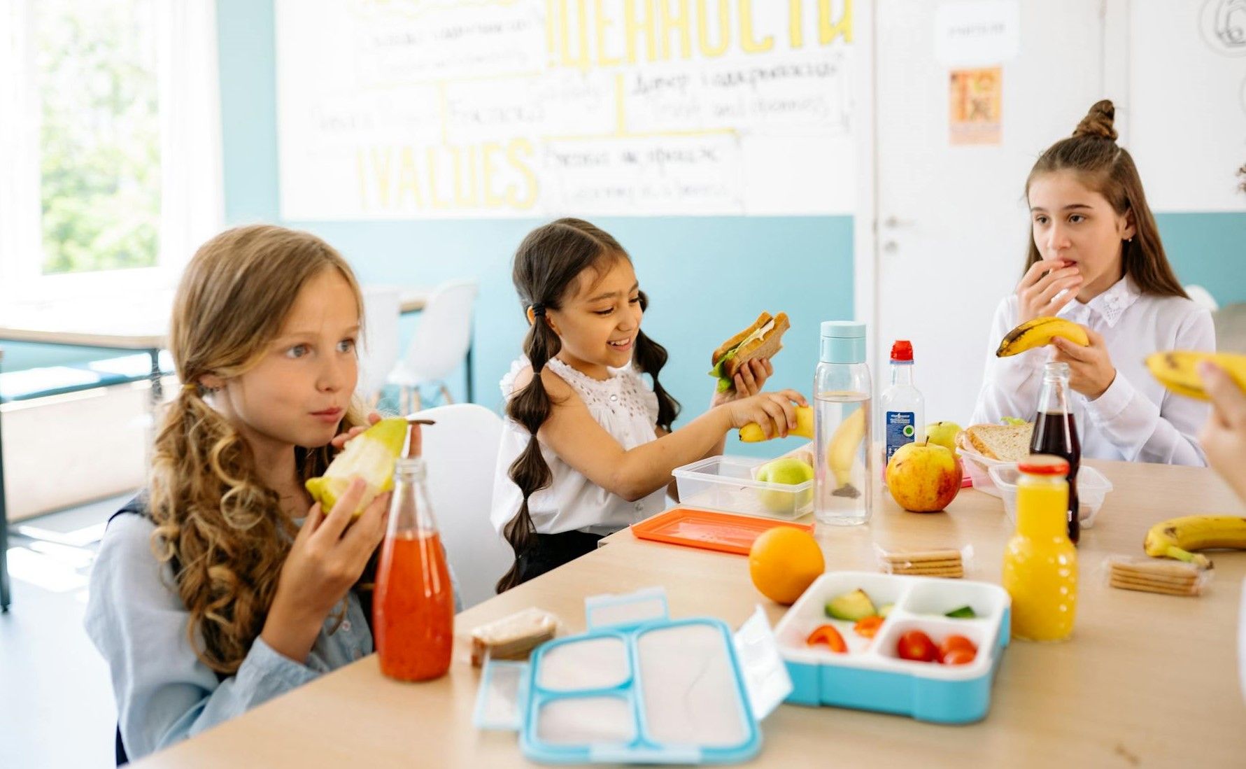 Primary school kids eat from their lunchbox around a table.