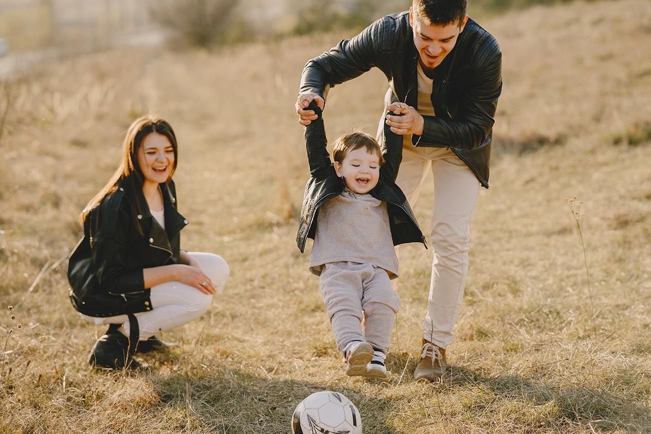 dad swinging toddler in park with mum watching smiling