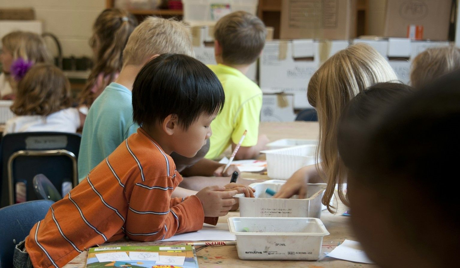 Child colours in at school while being surrounded by other kids.