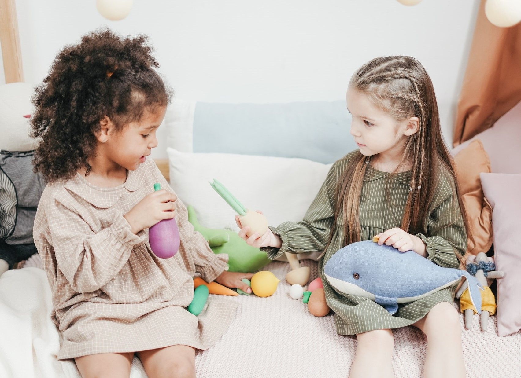 Two girls sit on bed and play with toys.